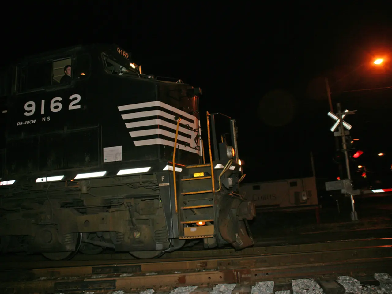 In this picture I can observe a train on the railway track. On the right there is a pole and a red...
