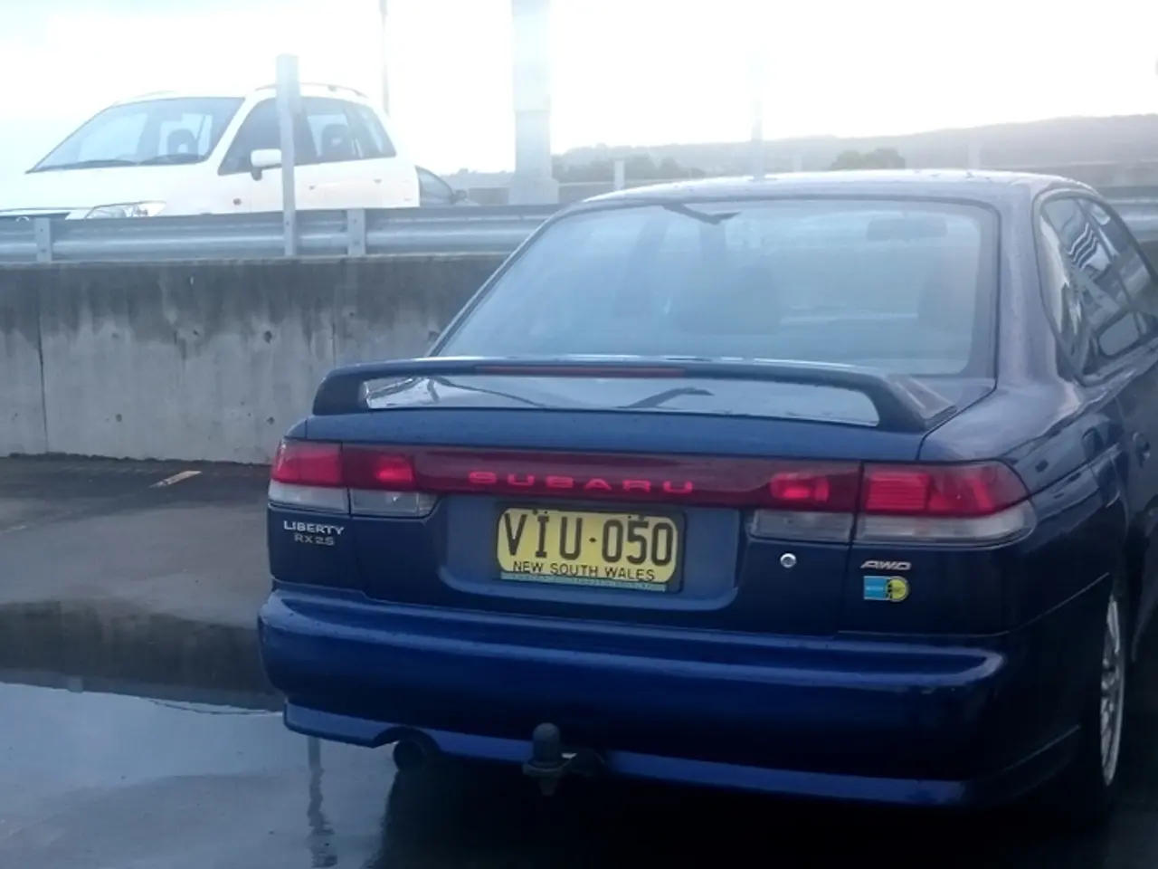 In this image I can see few cars and few poles. Here I can see yellow colour number plate and on it...