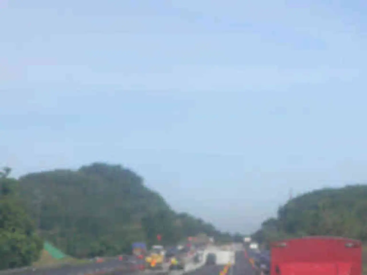 In the image there is a road, on the road there are traffic cones, dividers and vehicles. Around...