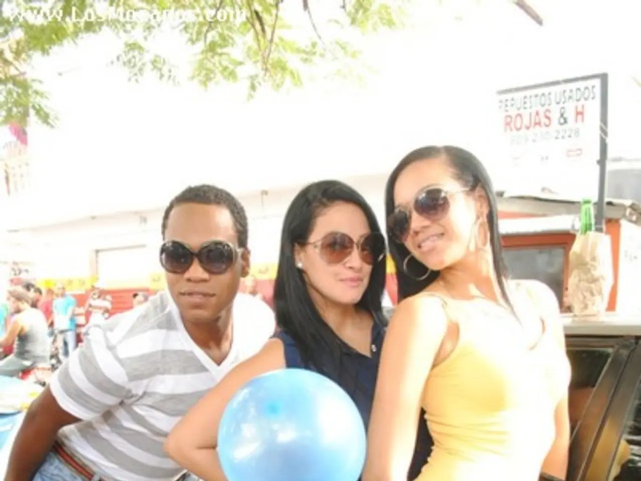 In this image there are three women standing on the road. The woman in the center is holding a...