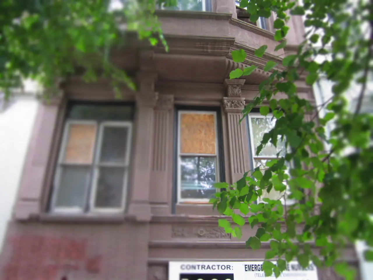 In this image there is a building having a board attached to it. On the board there is some text....