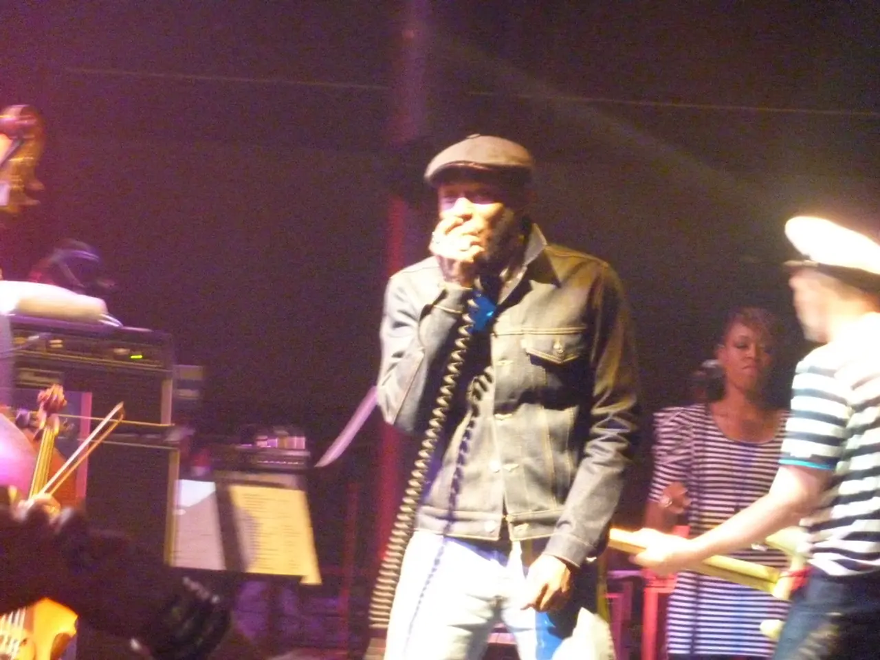 This person is holding a mic and singing and he wore jacket and cap. This is speaker, above this...