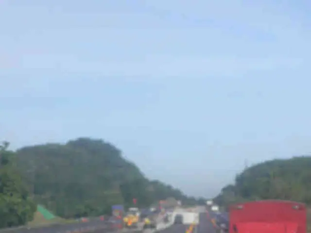 In the image there is a road, on the road there are traffic cones, dividers and vehicles. Around...