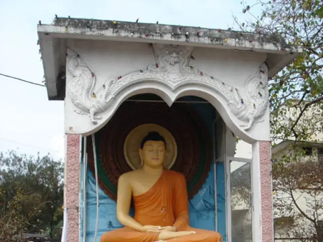 Here we can see a statue. Background there are trees, vehicle and building.