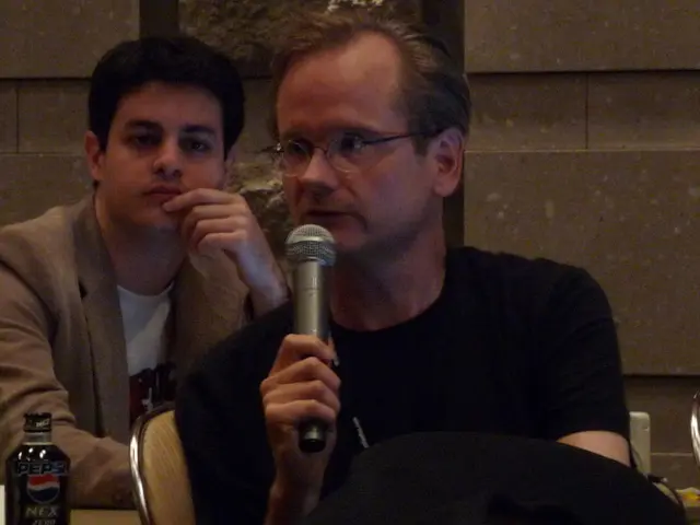 In this image I can see two people sitting on the chairs Among them one person is wearing the...