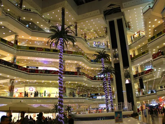 This is an inside view of an shopping complex, where there are trees, umbrellas with the poles,...