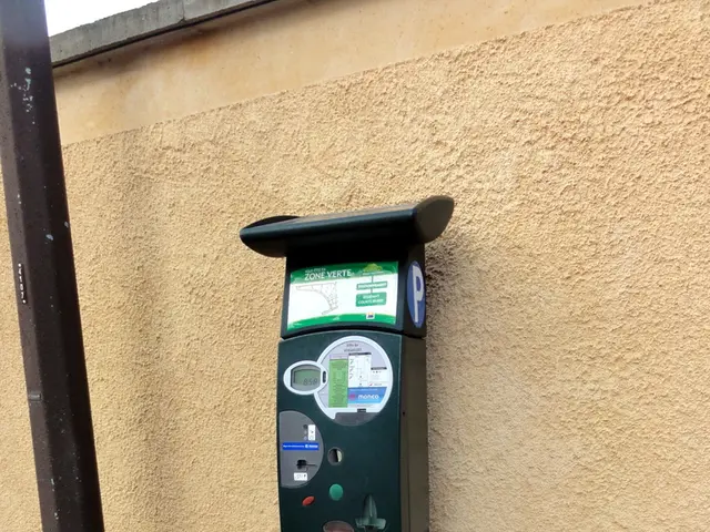 In the image there is an atm machine in front of the wall beside a pole.