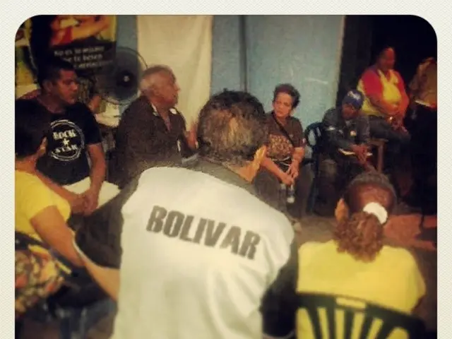 In this picture we can see a group of men and women sitting in the hall and discussing something....