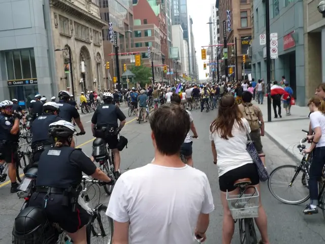 As we can see in the image there are buildings and few people riding bicycles on road.